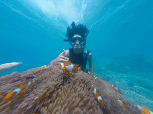 woman snorkeling with clownfish while giving a thumbs-up