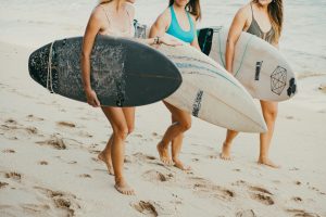 three women carrying surfboards along the beach