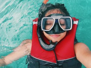 woman wearing a life jacket and a snorkeling mask taking a selfie while afloat