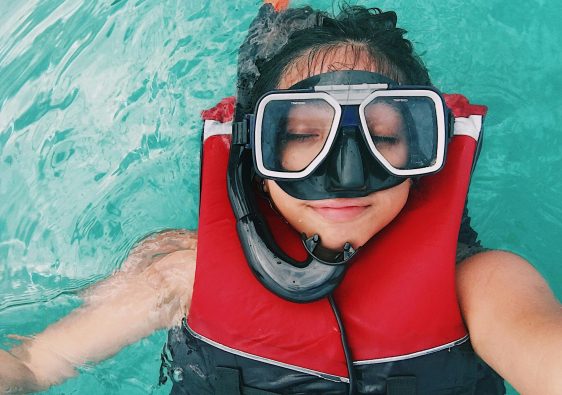woman wearing a life jacket and a snorkeling mask taking a selfie while afloat