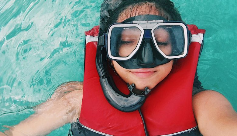 woman wearing a life jacket and a snorkeling mask taking a selfie while afloat